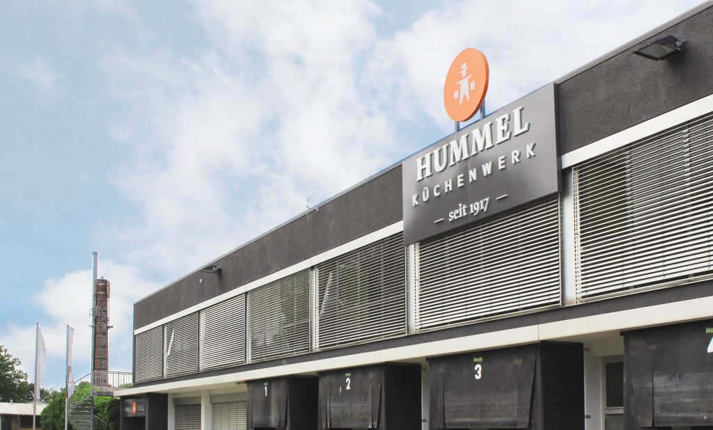 Fassade des Hummel Küchenwerks mit großem Logo. Flachdachbau aus den 70gern. Oben Büros unten Tore für Aus- und Anieferung.