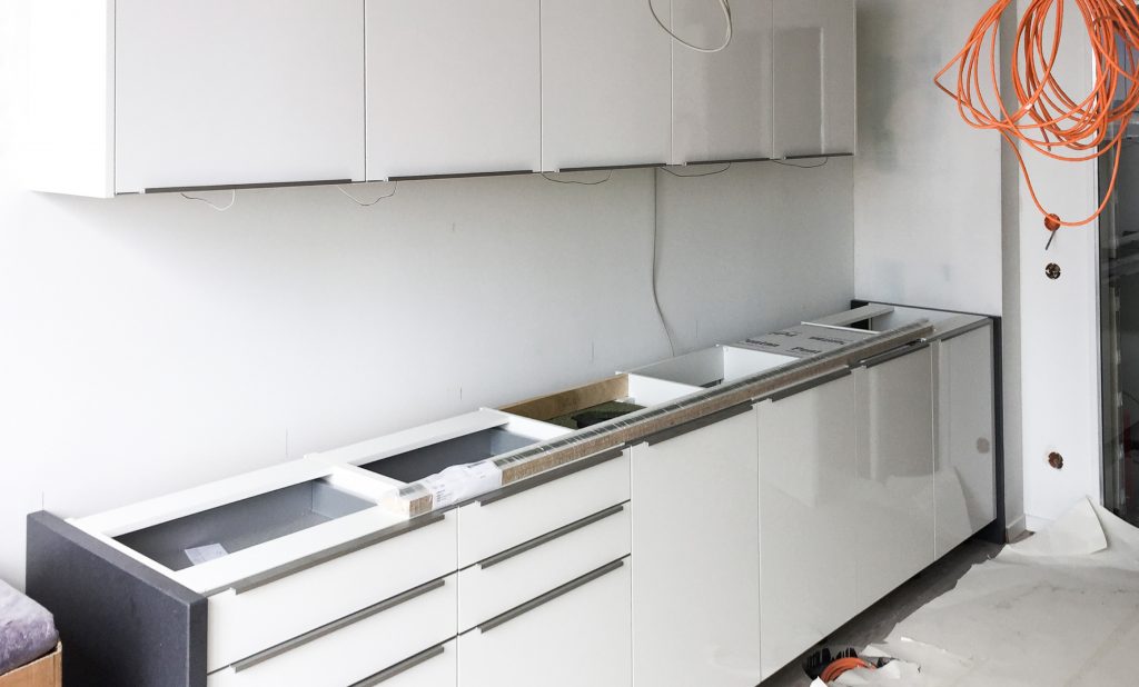 Weiße Hochglanzküche von Hummel-Küchen in einer noch nicht fertigen Wohnung. Arbeitsplatte fehlt. Kabel hängen herunter.