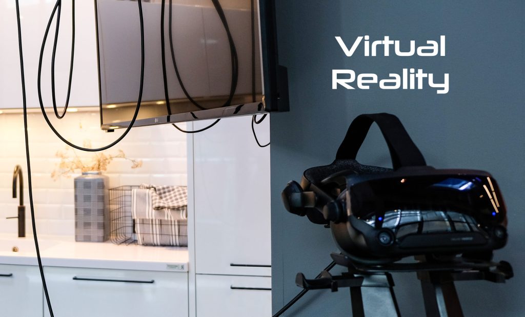 Links ist eine weiße Küchenzeile im Anschnitt zu sehen. Davor hängen Kabel von oben herunter und ein Bildschirm ist zu sehen. Rechts steht auf einer grauen Wand Virtual Reality und eine 3D-Brille auf einem Gestell in schwarz steht davor. Die Szene stammt aus einem Küchenstudio.