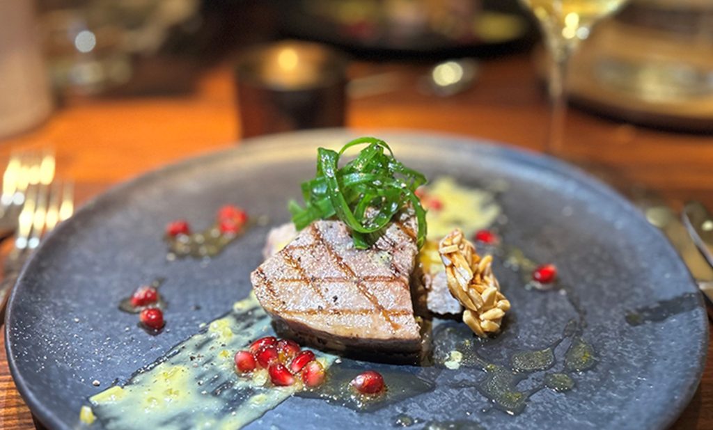 Teller mit gebratenem Thunfisch, Granatapfelkernen und grünen Algen auf schwarzem Teller.